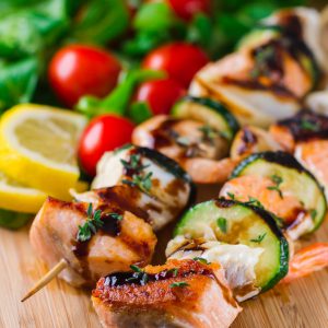 Brochettes de saumon, crevettes et légumes sur une planche.