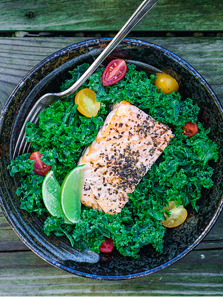 Kale caesar salad with grilled salmon, tomatoes, and lime.